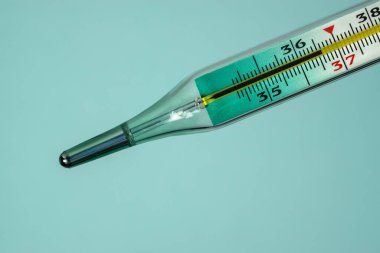 Tıbbi cam termometre normal vücut ısısını gösteriyor. Mavi arkaplanda yakın plan.