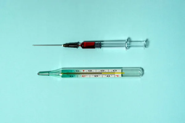 Lékařský teploměr ukazuje vysokou tělesnou teplotu. Skleněná injekční stříkačka s červenou tekutinou a jehlou. — Stock fotografie