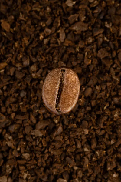 Um grão de café macro sobre um fundo de café moído — Fotografia de Stock