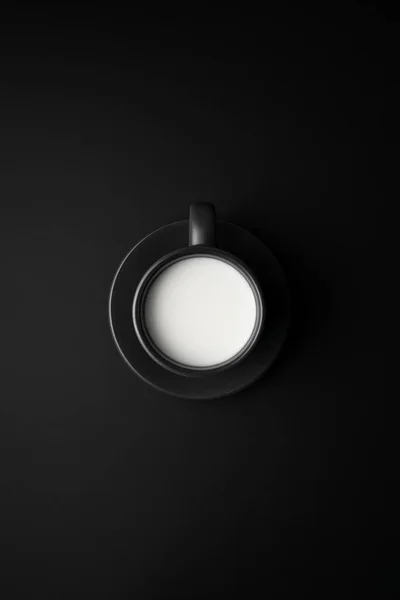 Mléko v černém šálku a podšálku na černém povrchu. — Stock fotografie