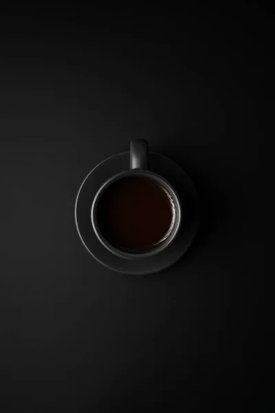 Black coffee in black cup and saucer on a black surface. — Stock Photo, Image