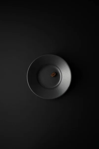 Un grano de café en platillo negro sobre una superficie negra . —  Fotos de Stock