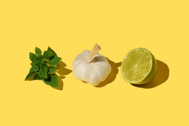 Fesleğen yaprakları, sarımsak soğanları, arka arkaya sarı arka planda koyu gölgeli yarım limon.