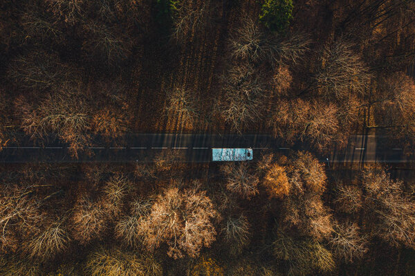 Вид с воздуха на небольшую асфальтированную лесную дорогу, вождение автомобилей осенью
. 