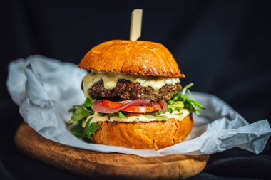 Koyu arkaplanda ahşap tabakta servis edilen mavi peynirli ev yapımı sığır eti burgeri. 