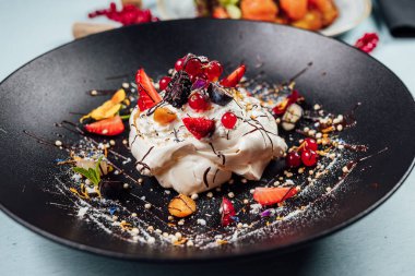 Pavlova kekleri taze ahududu ve yaban mersini ile birlikte restoranda koyu tabakta. 