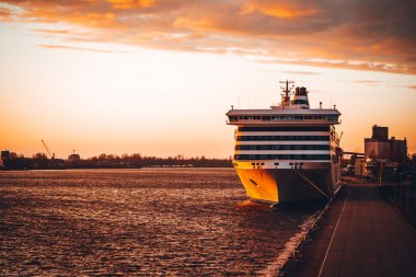 Gün batımında küçük bir kasabadaki rıhtımın yanındaki yolcu gemisinin ön tarafında..