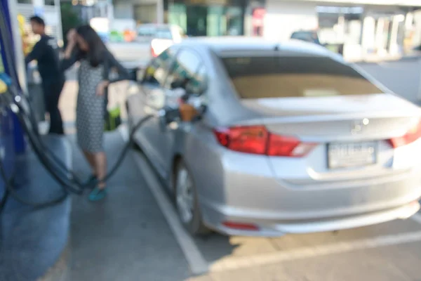 Imagen borrosa sosteniendo la boquilla de combustible y el coche de repostaje en la gasolinera —  Fotos de Stock