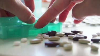 Kadın ilaç organizatörünü açar ve beyaz ve kahverengi hapları ayırır. Makro