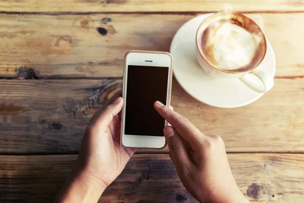 woman's hands holding mobile smart phone with hot coffee cup at cafe shop