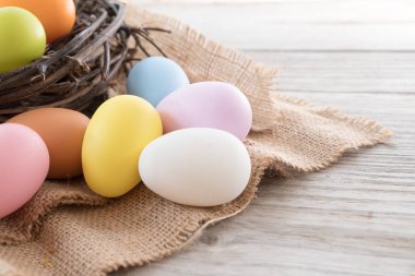 Yuvaya çiçek rustik ahşap plakalar arka plan üzerinde renkli Paskalya yumurtaları. Bahar mevsimi tatil. Vintage pastel renk tonu. Kompozisyon kadar kapatın.