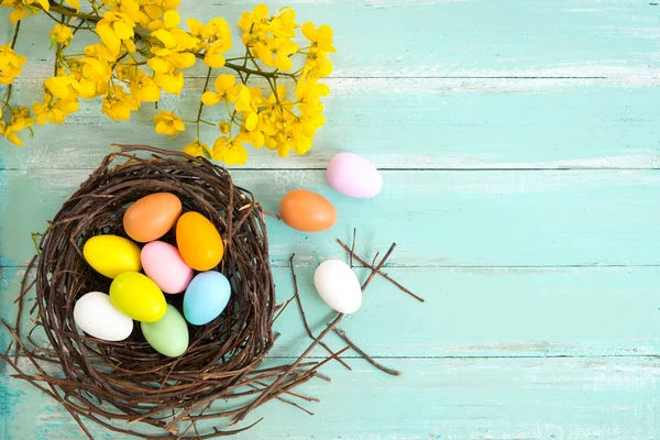 Yuva çiçek rustik ahşap plakalar arka planda mavi boya ile renkli Paskalya yumurta. Bahar mevsimi tatil. Vintage renk tonu stili. Üstten Görünüm kompozisyon.