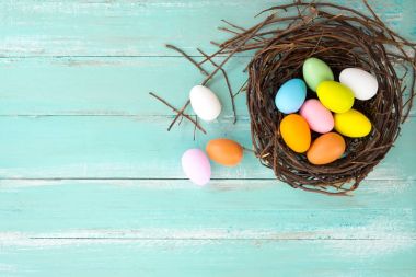 Yuva çiçek rustik ahşap plakalar arka planda mavi boya ile renkli Paskalya yumurta. Bahar mevsimi tatil. Vintage renk tonu stili. Üstten Görünüm kompozisyon.
