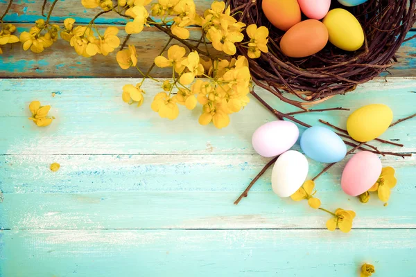 Yuva çiçek rustik ahşap plakalar arka planda mavi boya ile renkli Paskalya yumurta. Bahar mevsimi tatil. Vintage renk tonu stili. Üstten Görünüm kompozisyon.