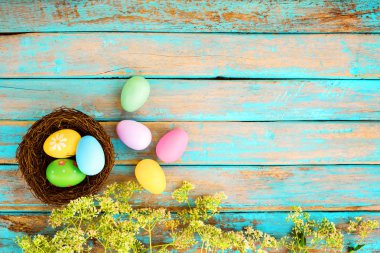 Yuva çiçek rustik ahşap plakalar arka planda mavi boya ile renkli Paskalya yumurta. Bahar mevsimi tatil. Vintage renk tonu stili. Üstten Görünüm kompozisyon.