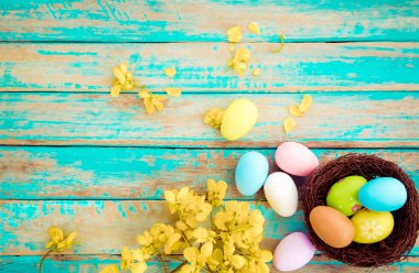 Yuva çiçek rustik ahşap plakalar arka planda mavi boya ile renkli Paskalya yumurta. Bahar mevsimi tatil. Vintage renk tonu stili. Üstten Görünüm kompozisyon.