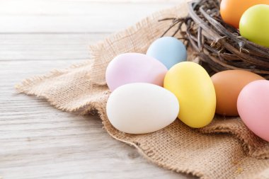 Yuvaya çiçek rustik ahşap plakalar arka plan üzerinde renkli Paskalya yumurtaları. Bahar mevsimi tatil. Vintage pastel renk tonu. Kompozisyon kadar kapatın.