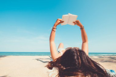 Eğlence yaz - genç kadın tropikal bir kumsalda yatıp kitapla rahatlayın. Mavi deniz içinde belgili tanımlık geçmiş. Yaz tatil kavramı. Vintage renk tonu.