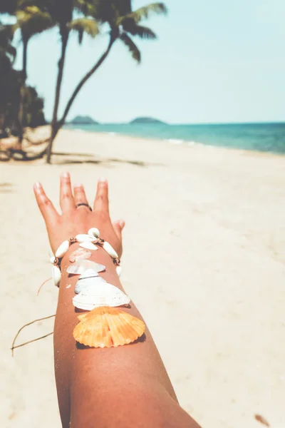 Relaxation and Leisure in summer - Seashell on tanned girl arm at tropical beach in summer. vintage color tone