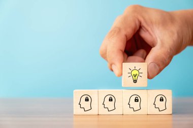 Business concept of creative idea and innovation. Hand picked wooden cube block with light bulb icon (new idea) over wood block with unlock icon and head human symbol have no idea.