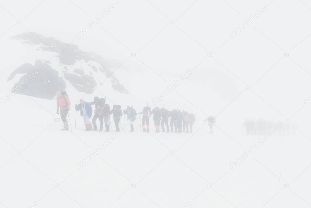 Group of climbers climbing snowy mountain peaks in dense fog.