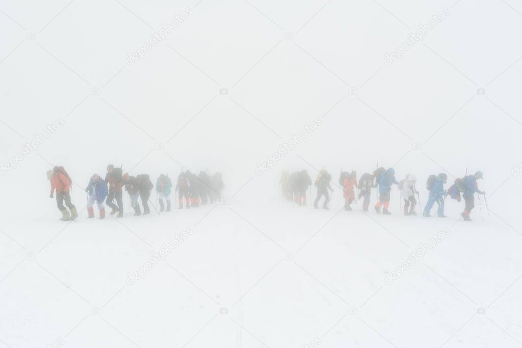 Group of climbers in the fog climbing the snowy mountain peaks.