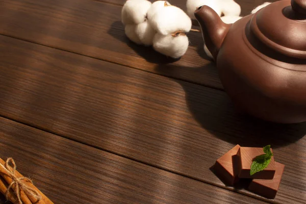 Kahverengi kil çaydanlık, nane, çikolata şekeri, tarçın ve kahverengi ahşap arka planda pamuk. Üst görünüm.