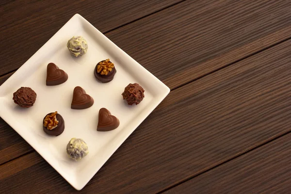 Various types of chocolate sweets arranged on a plate on a brown wooden background