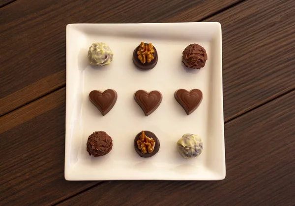 Various types of chocolate sweets arranged on a plate on a brown wooden background