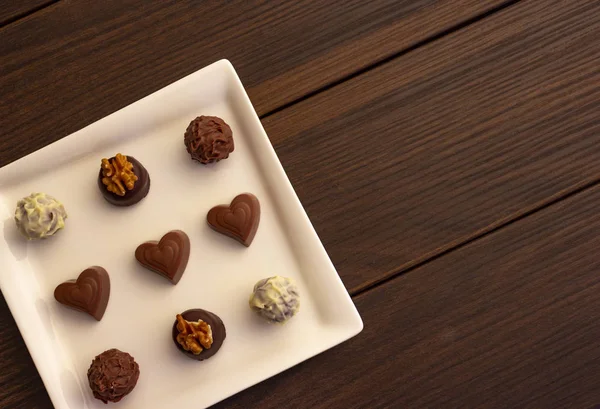 Various types of chocolate sweets arranged on a plate on a brown wooden background
