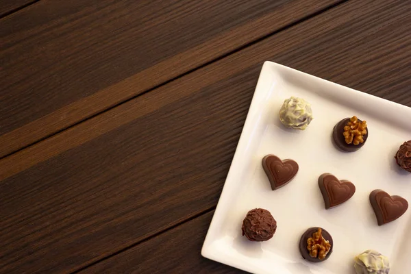 Various types of chocolate sweets arranged on a plate on a brown wooden background
