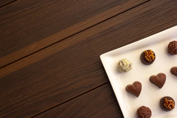 Various types of chocolate sweets arranged on a plate on a brown wooden background