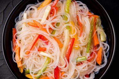 Erişte. Siyah tabakta sebzeli Funchoza. Japon yemeği. Kore yemeği. Çin mutfağı. Geleneksel yiyecekler.