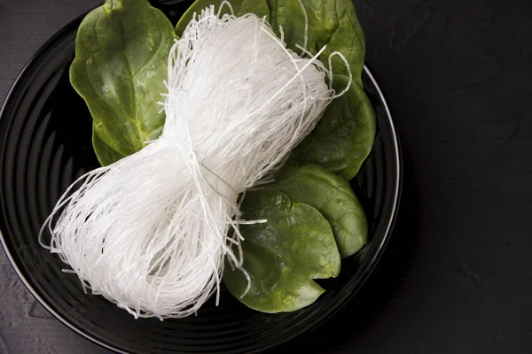 Asian food. Noodles in a black plate with herbs. Not ready funcheza.copy space