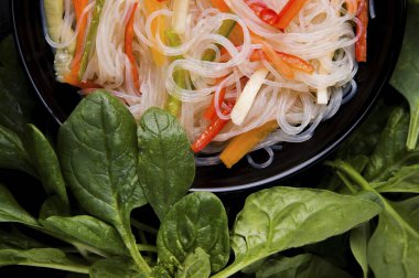 Siyah arka planda havuçlu ve biberli erişte. Yakınlarda fesleğen yaprakları, yeşiller var. Asya yemekleri. Funcheza.