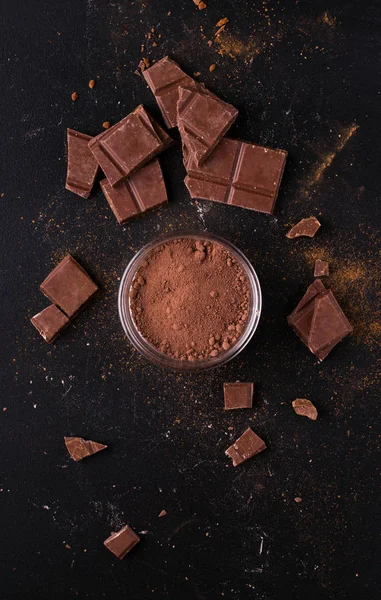 Kakaový prášek na černém pozadí vedle čokolády a skořice. — Stock fotografie