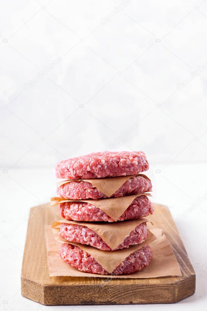 raw frozen minced meat patties on a wooden board, on a white background. copy space. Vertical image