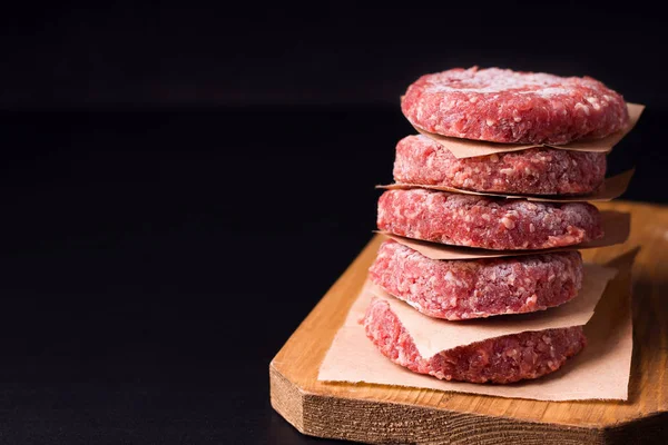 Carne picada cruda congelada en forma de chuletas sobre un fondo negro. tener espacio de copia — Foto de Stock