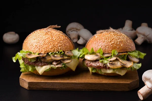 sandwich with beef and mushrooms on a wooden board on a black background next to fresh mushrooms
