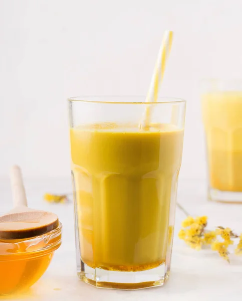 Susu emas dalam gelas dengan sedotan dengan latar belakang putih di sebelah madu. Minuman tradisional India. — Stok Foto