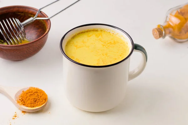 Golden milk in a mug on a white table in the cooking process. — Stock Photo, Image