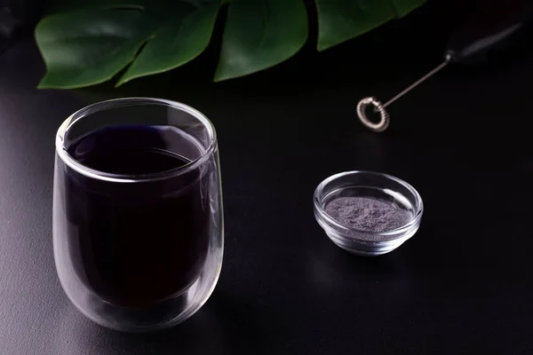 Té matcha azul sobre un fondo negro en un vaso junto a una batidora y polvo seco —  Fotos de Stock