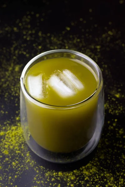 green matcha iced tea in a glass on a black background