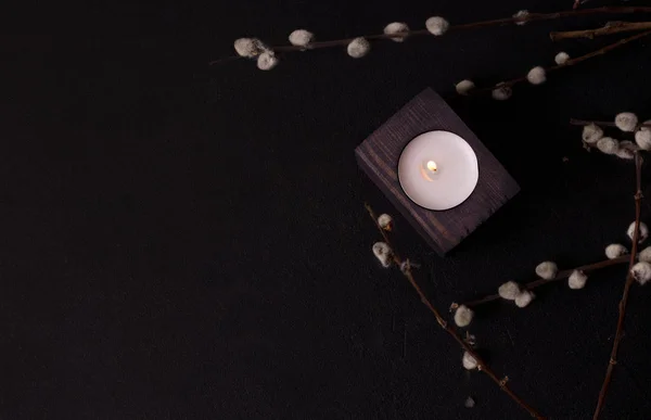 one candle in a wooden candlestick in willow branches on a black background. dark environmental design
