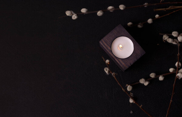 одна свеча в деревянном подсвечнике в ивовых ветвях на черном фоне. темный дизайн окружающей среды
