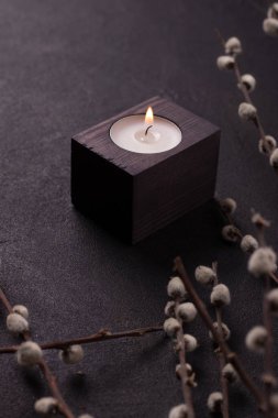 Kara arka planda, dalların yanında, ahşap bir şamdanda mum yakmak. Koyu bir tasarımın dikey fotoğrafı