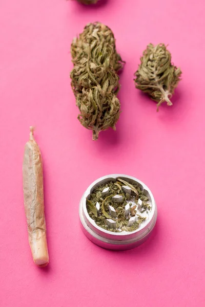 A jamb with marijuana and whole hemp next to a grinder on a pink background — Stock Photo, Image