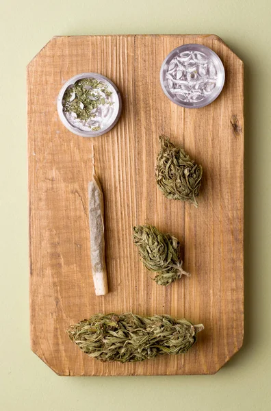 Marijuana su una tavola di legno asciutta e tagliuzzata accanto a una sigaretta con marijuana — Foto Stock