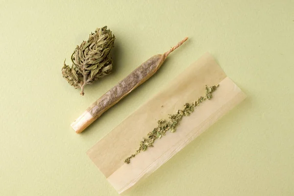 Der Prozess der Herstellung einer Rolle Zigaretten mit Marihuana auf grünem Hintergrund — Stockfoto
