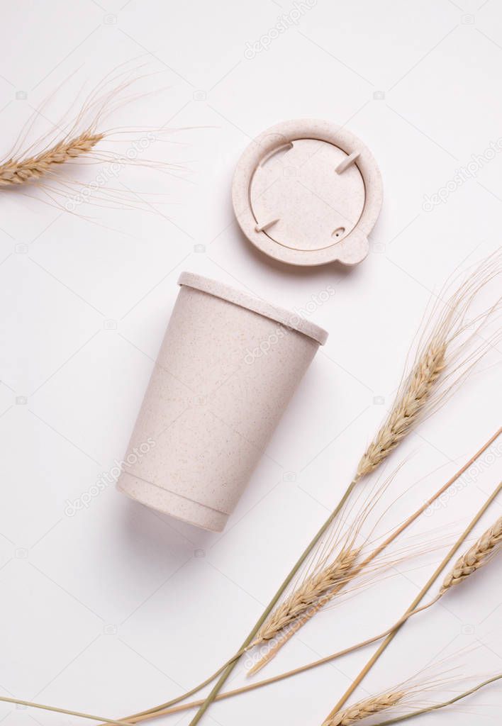 reusable coffee cup on a white background next to ears of wheat.